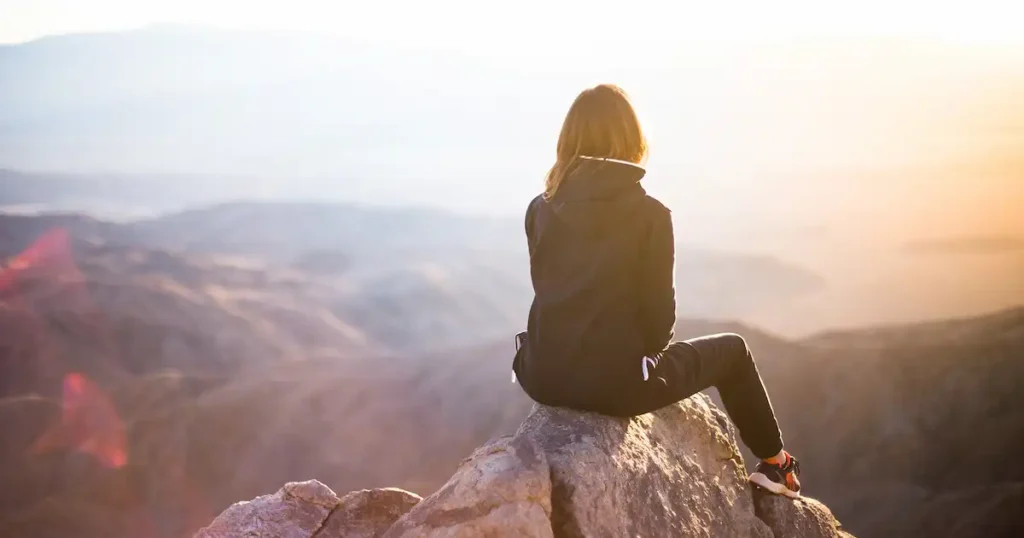 mujer subida en un montículo montañoso buscando fe cristiana